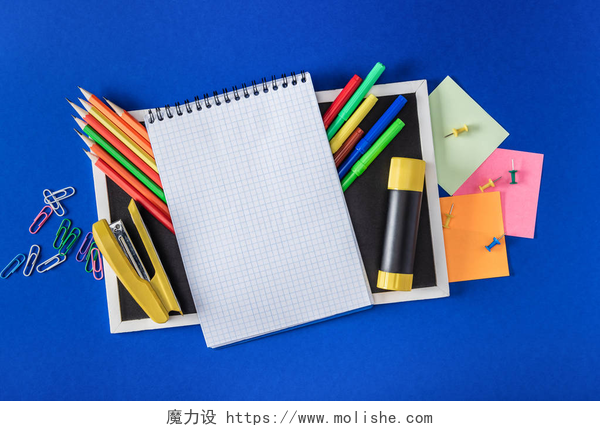 白色桌子上的各种文具空白笔记本和蓝色背景的各种信纸的空黑板的顶部视图 
